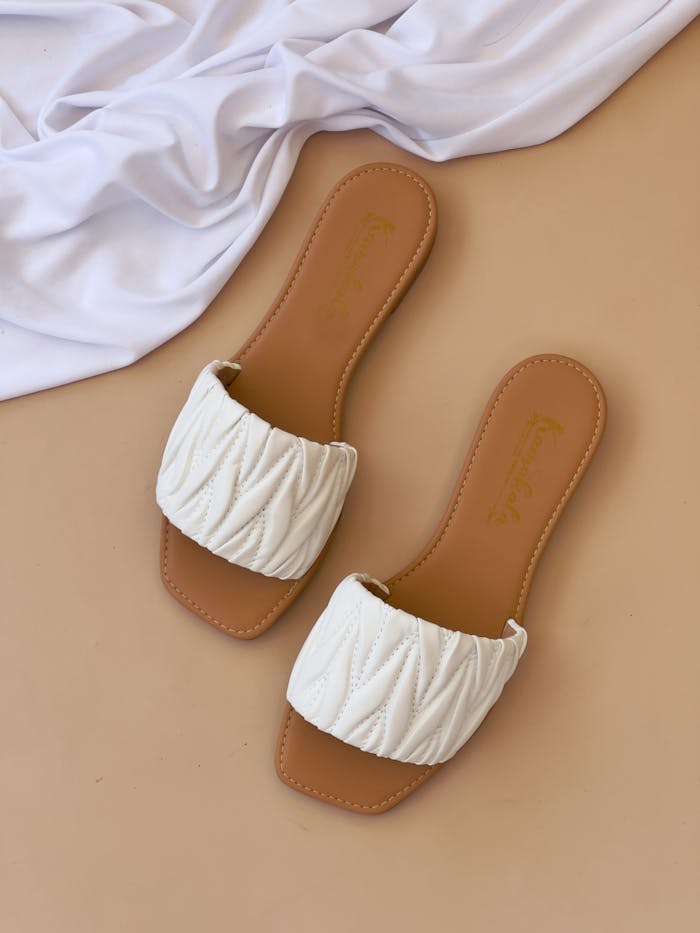 services-02 Stylish white quilted slippers on a beige background with white cloth accent.