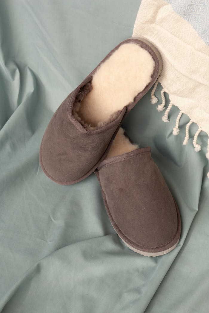 services-03 Pair of cozy brown slippers with cream lining on soft blue fabric setting.